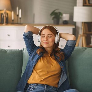 Serene young woman enjoying music through headphones, finding tranquility on her comfortable sofa